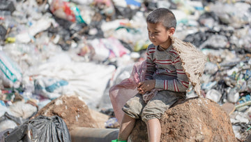 A young boy sits with a pink plastic bag with a mountain of landfill around him
