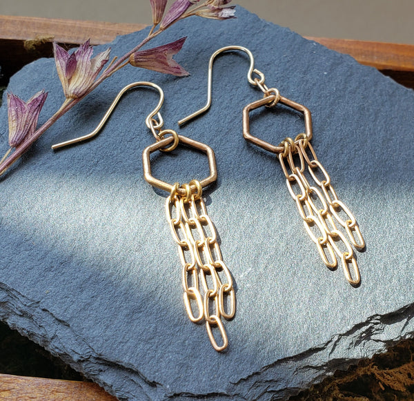small bronze hexagons with bronze chains fringe on gold fill ear wires slate background with dried flower