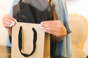 two manicured hands holding a kraft boutique shopping bag