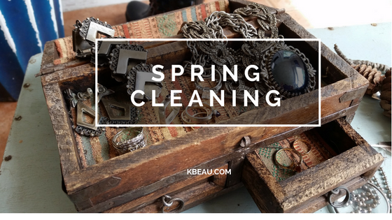 A wooden, rustic box has a variety of jewelry in it like a necklace with a large hematite pendant, a pair of vintage sterling silver clip on earrings and a simple, delicate gold ring