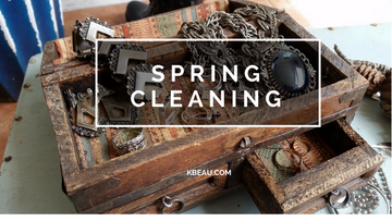 A wooden, rustic box has a variety of jewelry in it like a necklace with a large hematite pendant, a pair of vintage sterling silver clip on earrings and a simple, delicate gold ring