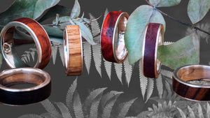 six silver bands with wooden inlay. Some of the inlays are deep red, others are light brown. The background is eucalyptus and black and white fern. The blog post is about the pitfalls of alternative wedding bands