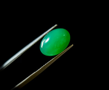 oval chrysoprase cabochon held in tweezers