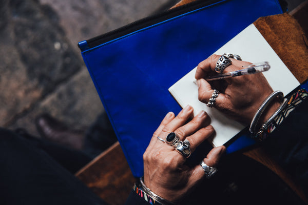 image for kbeau blog post about why jewelry turns your skin green black. The image is a man's hands. He's wearing lots of big silver rings, some have gemstones. And he is writing in a small journal.