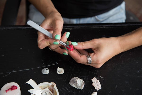 woman's hands with seafoam green nail color is holding a piece of red wax that she is carving