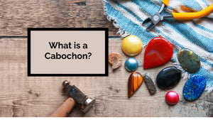 a wide variety of cabochons on a wooden tabletop background. A hammer and pair of pliers are lying on the table too.