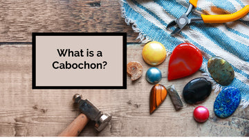 a wide variety of cabochons on a wooden tabletop background. A hammer and pair of pliers are lying on the table too.