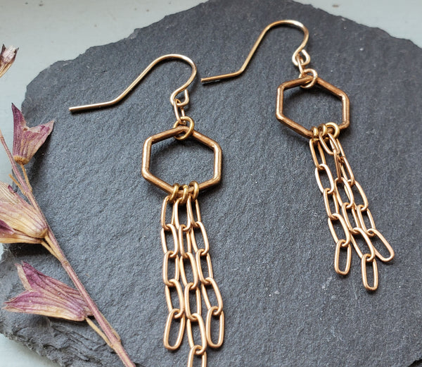 small bronze hexagons with bronze chains fringe on gold fill ear wires slate background with dried flower