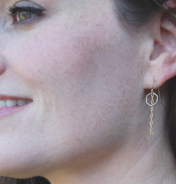 woman smiling and wearing earrings of tiny hexagons with a gold chain hanging down with a bead of citrine at the end like a honey drop
